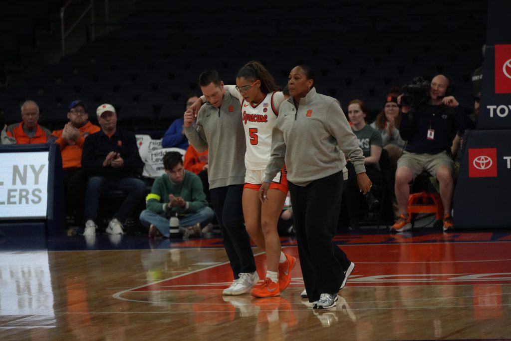 Leila Filia, wearing a white Syracuse uniform, is helped off the court by two staff members after sustaining an injury during the game against Cal at the JMA Wireless Dome.