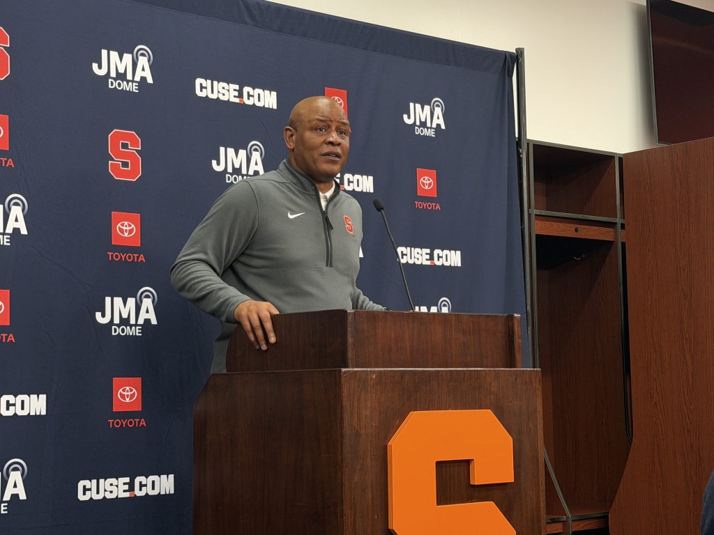 Syracuse basketball coach at podium speaking into microphone